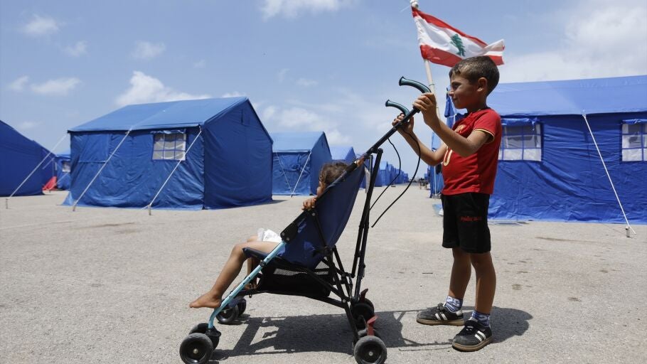 22 de mayo de 2026, Beirut, L&iacute;bano: Un ni&ntilde;o desplazado tira de un peque&ntilde;o carro en el que transporta a su hermana menor entre las filas de tiendas de campa&ntilde;a azules instaladas por el Gobierno liban&eacute;s para acoger a las familias desplazadas de Beirut.
