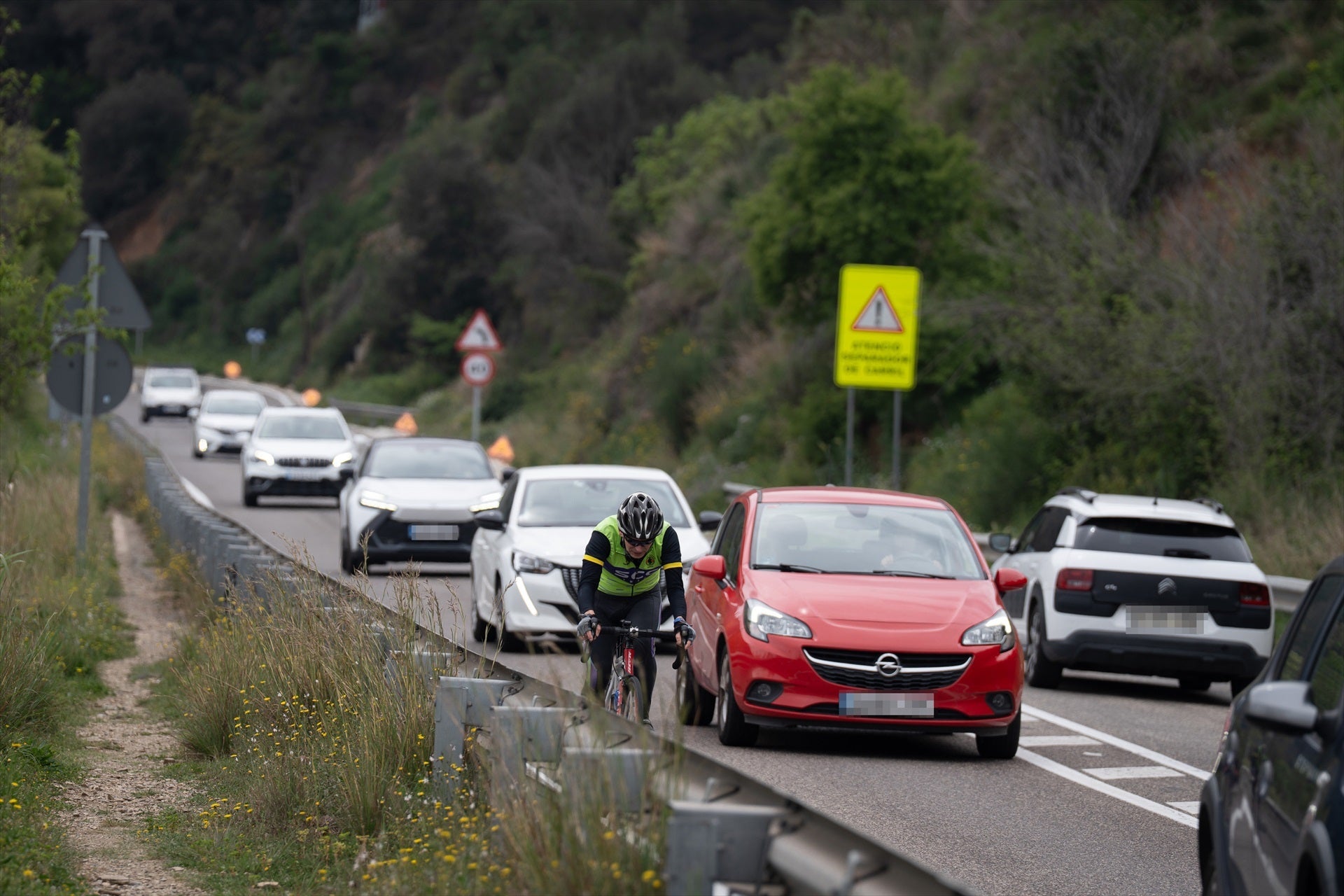 Una carretera de Cataluña en la que hay multitud de coches y un ciclista por el arcén Una carretera de Cataluña en la que hay multitud de coches y un ciclista por el arcén